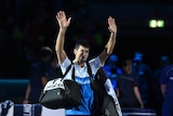 A tennis player holds his hands above his head in salute and a farewell to the crowd after losing a match.