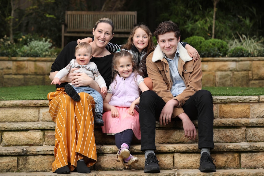 A family sits on backyard steps- mother and two girls, teenage son and baby