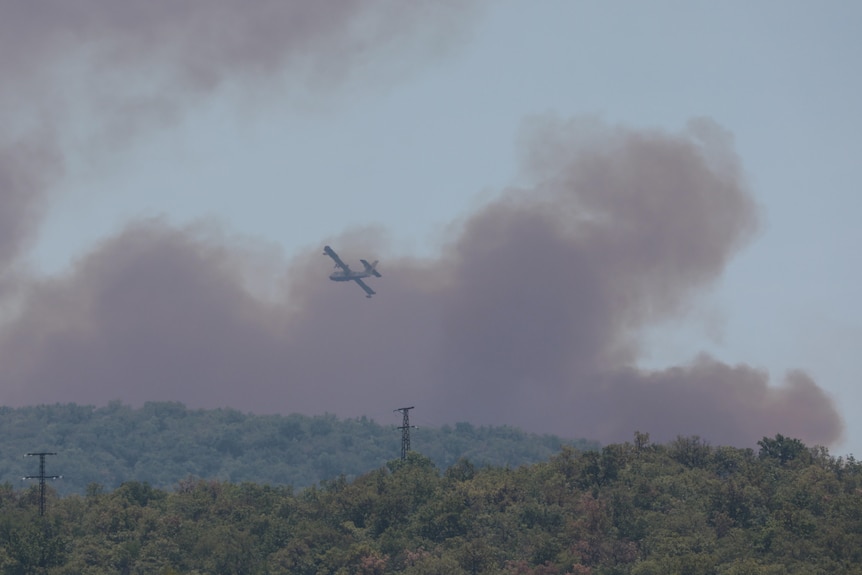 Aereo in aria con grandi nuvole di fumo sullo sfondo. 