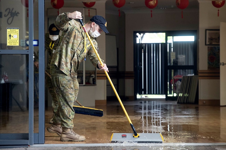 A soldier uses a large broom to sweep water out of a building.