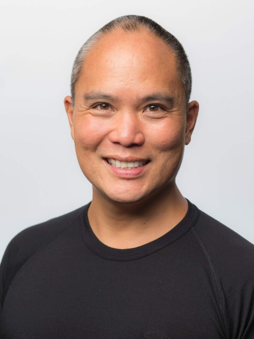 A man with close-cropped hair and a black t-shirt smiles into the camera.