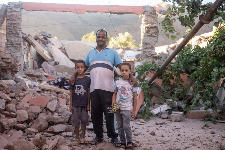 A dad and his two sons stand amidst a pile of rubble.