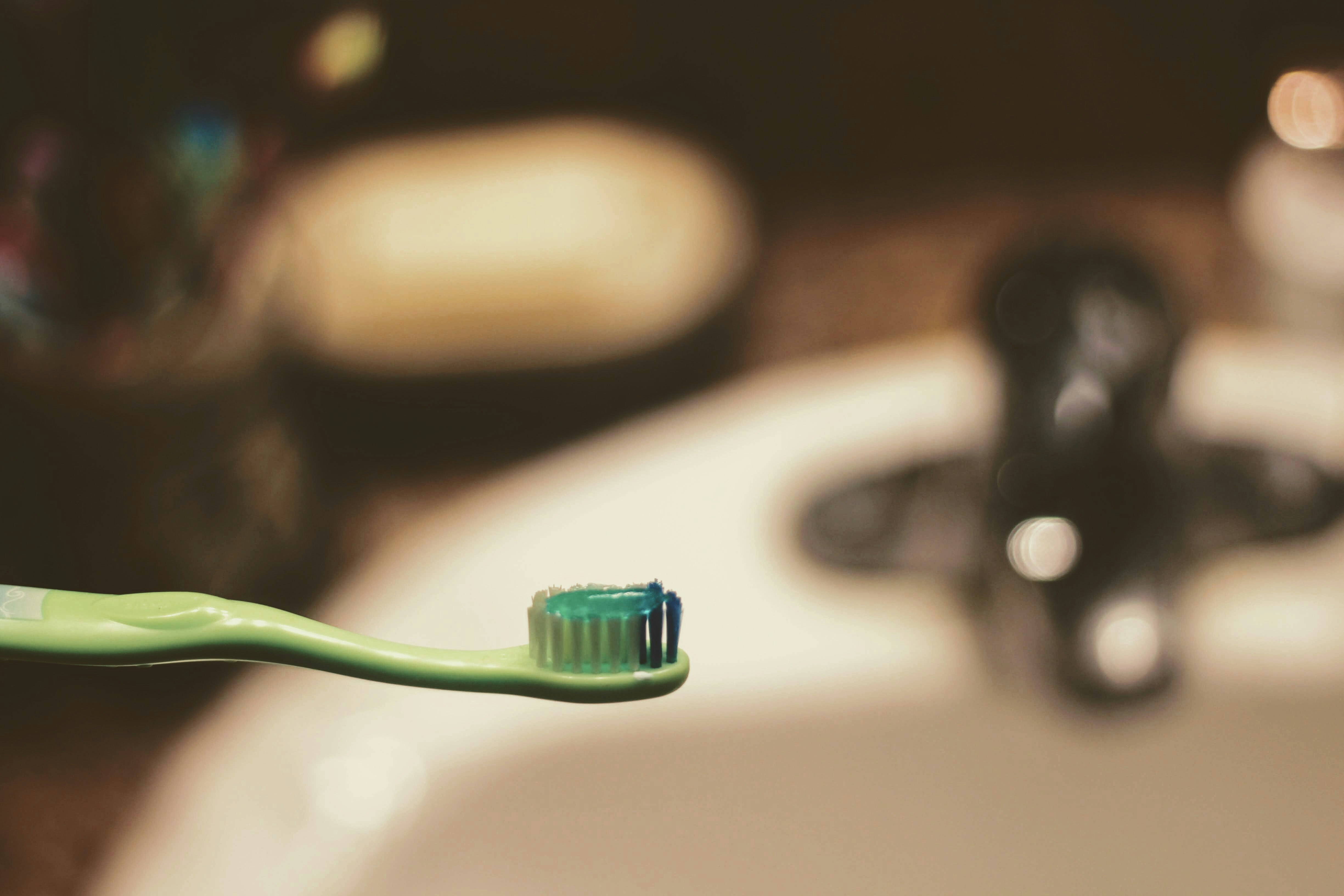 A green toothbrush loaded with green toothpaste in front of a bathroom sink.