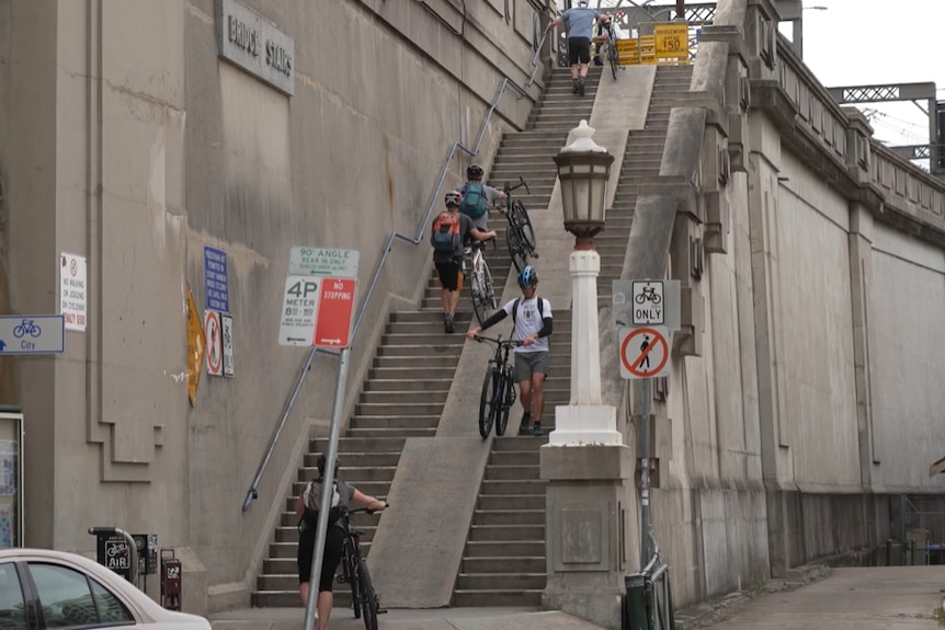 Cyclists carry bikes up stairs at Sydney Harbour Bridge