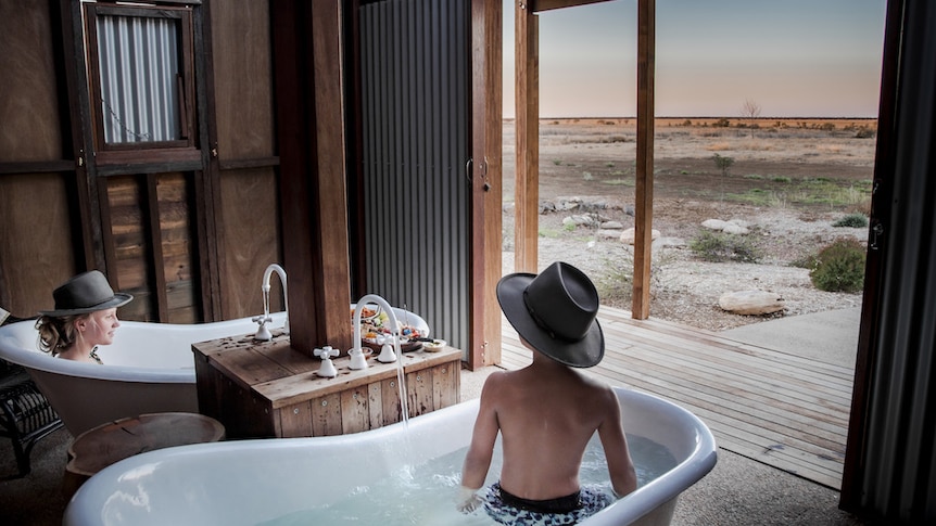 a shed in the middle of the outback with two baths inside and people enjoying the view