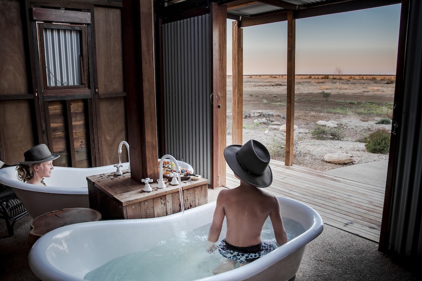 a shed in the middle of the outback with two baths inside and people enjoying the view