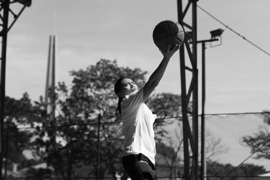 A black and white photo of Kat Tan doing a layup on an outdoor basketball court.