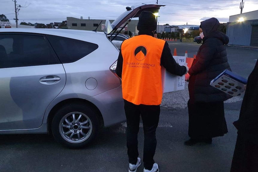 Two people are putting a box in an opened car boot