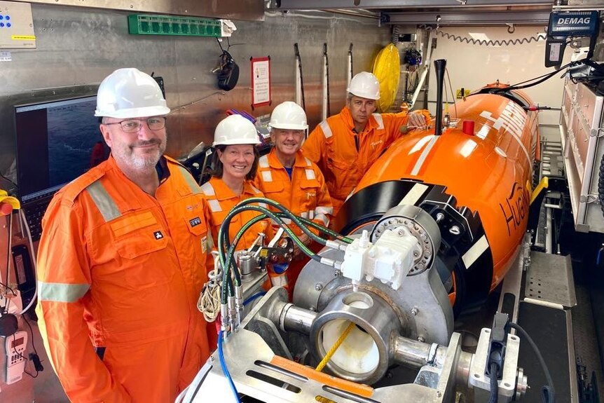 A group of people in high-vis outfits stands next to an underwater vehicle.