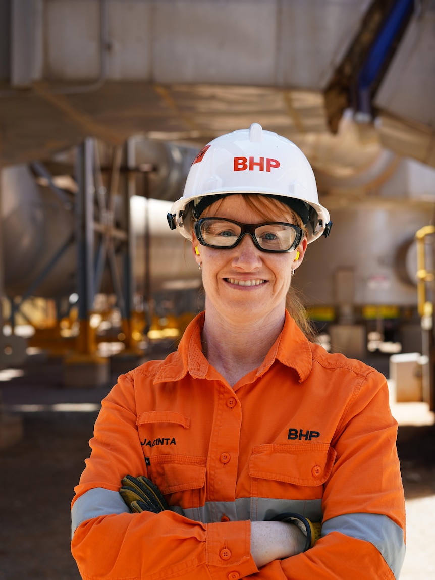 A woman wearing high-vis workwear and a hard hat and safety glasses on a mine site.  
