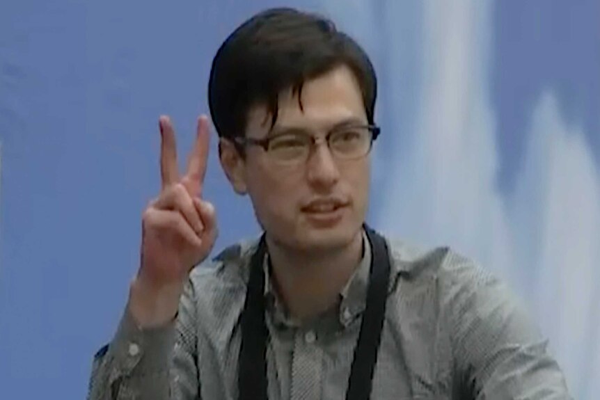 Alek Sigley holds up two fingers in the V for victory sign as he walks through an airport terminal.