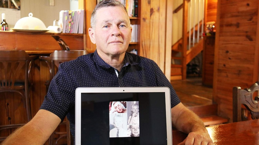 Gary Devitt sits at his dining room table in his home at New Farm in Brisbane, with photos of his missing brother Michael.