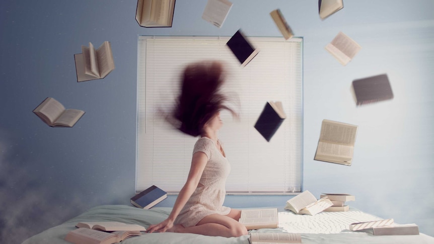 Woman sitting on bed in room, in apparent whirlwind. Her hair is fllying about, and she is surrounded by flying or falling books