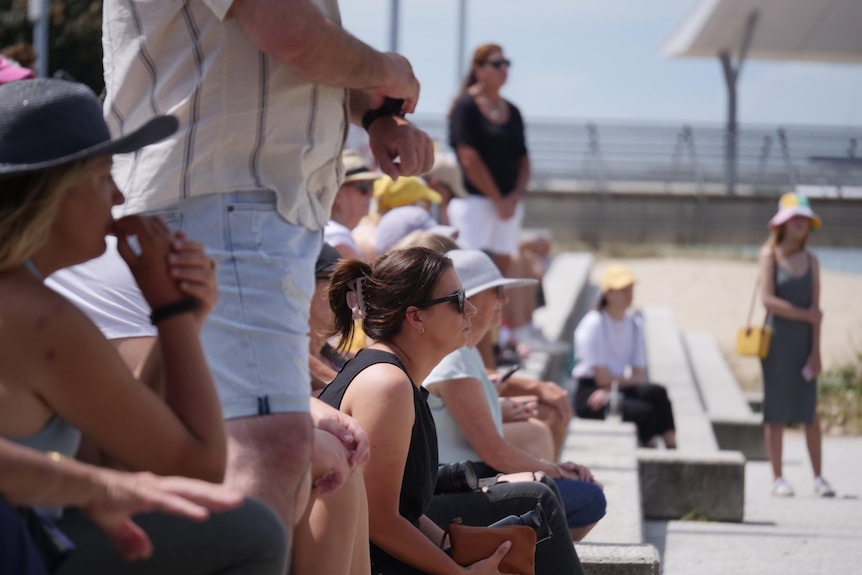 people sit on stairs and stand during a public vigil on the Gold Coast