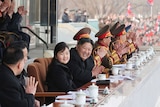 A beaming, heavy Korean man claps as he sits alongside a number of generals and a young, smiling Korean girl.