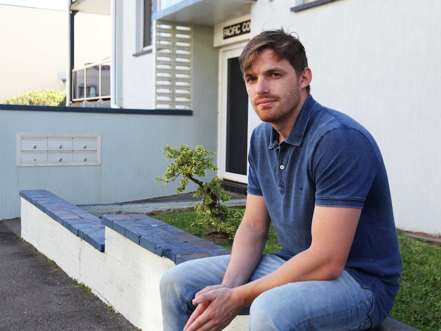 A young man sits outside his rental accommodation