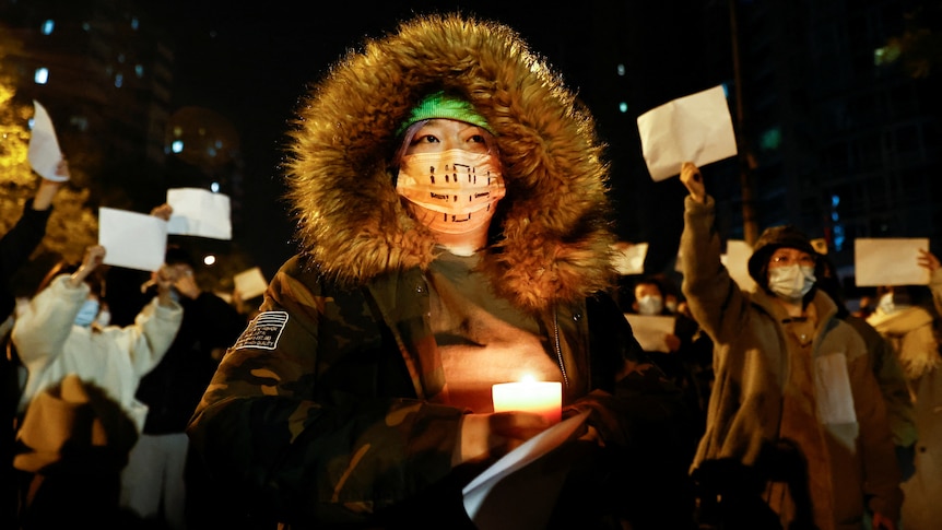 A person holds a candle, as people gather for a vigil and hold white sheets of paper in protest.