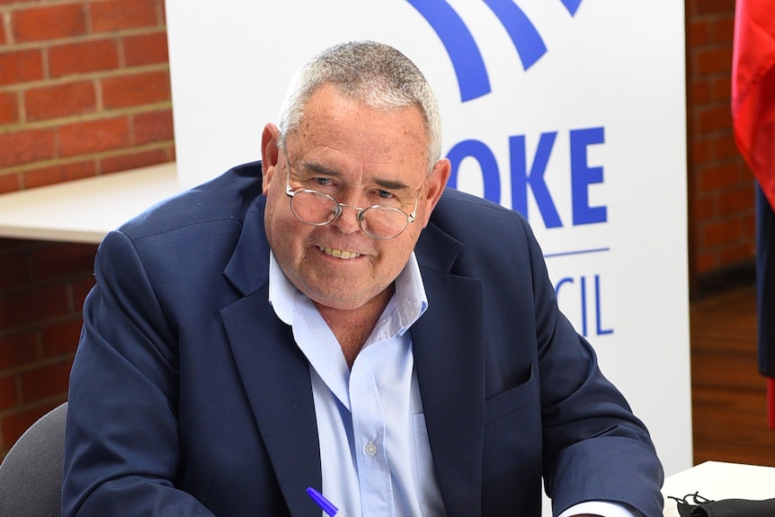 A politician in a dark suit sits at a table, smiling.