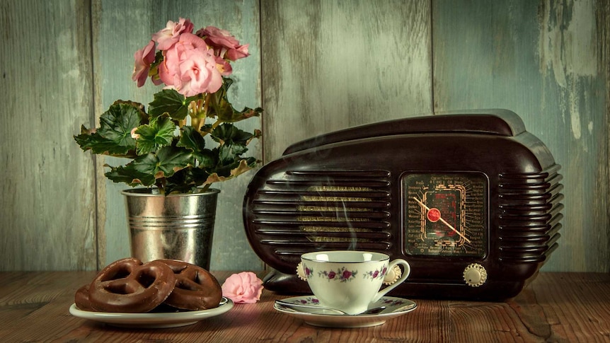 An old fashioned radio next to a cup of tea and plate of biscuits.