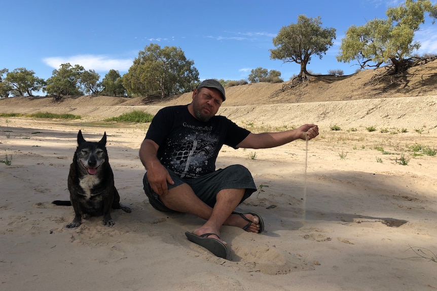 A man and a dog sitting in a dry river bed on a sunny day