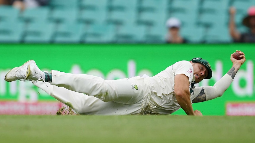 A fielder lies lengthwise on the ground, holding the ball in one hand after a great catch.