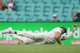 A fielder lies lengthwise on the ground, holding the ball in one hand after a great catch.