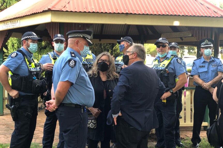 Police officers and a man in a suit speak to a small woman who is smiling up at them.