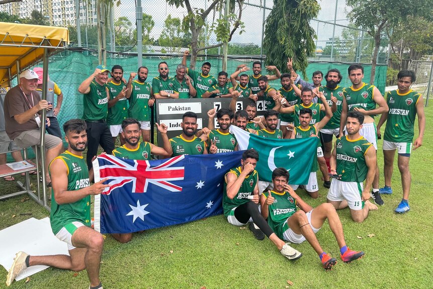 A group of footballers in green singlets gather around an Australian and Pakistani flag