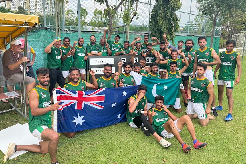 A group of footballers in green singlets gather around an Australian and Pakistani flag