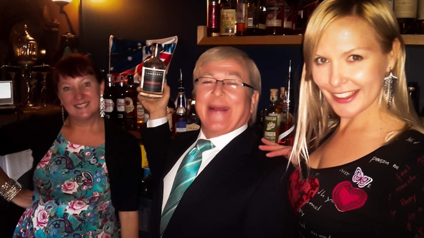 A Kevin Rudd impersonator stands between two women behind a bar