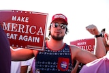 A man holds up a sign reading "make american great again" and flexes his muscles