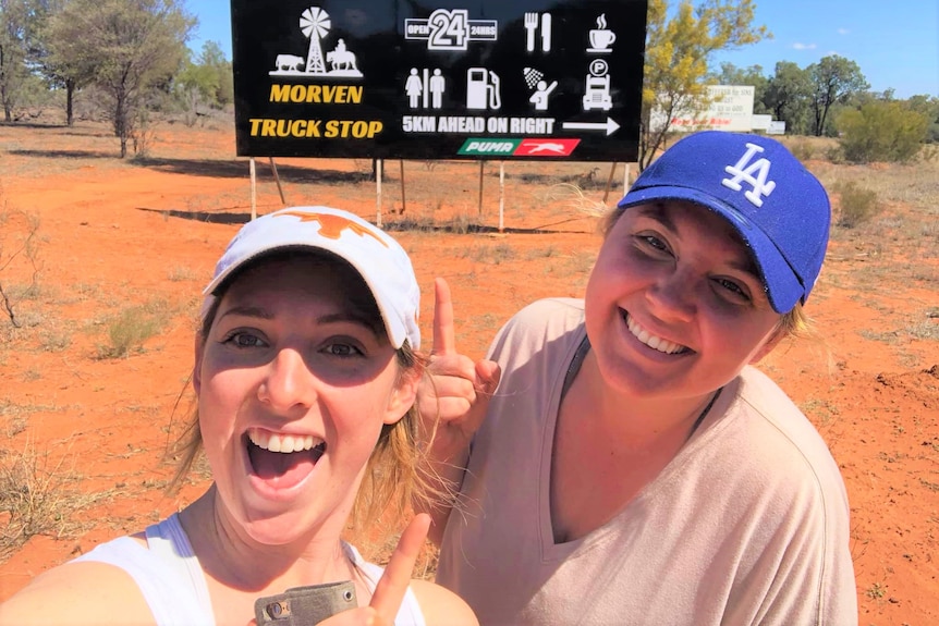 Two women smiling in front of the Morven Truck Stop Billboard