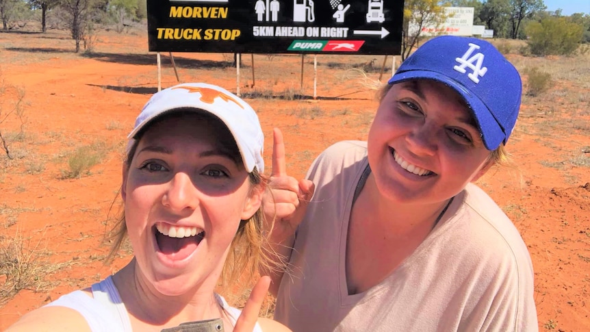 Two women smiling in front of the Morven Truck Stop Billboard