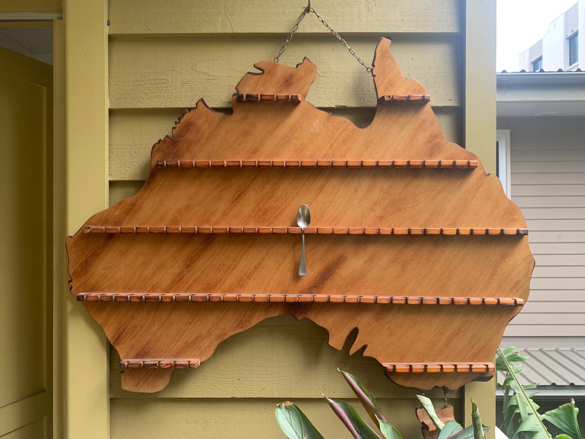 Brown wooden spoon display rack hanging on a yellow wall with one teaspoon in the middle.