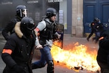 Riot police run past burning dustbins