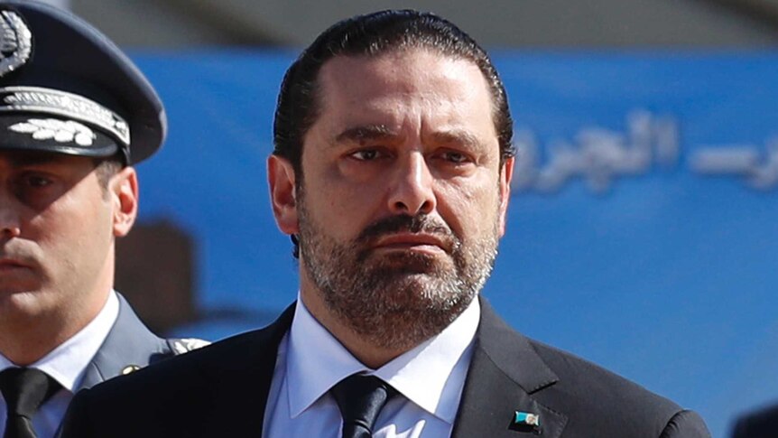 Lebanese Prime Minister Saad Hariri walks next to a military person.