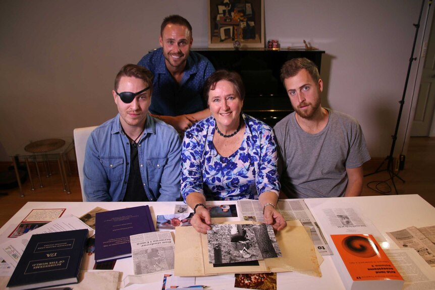 A wide shot showing Karen Goodall-Smith and her three sons smiling for a photo sitting at a table in a living room.