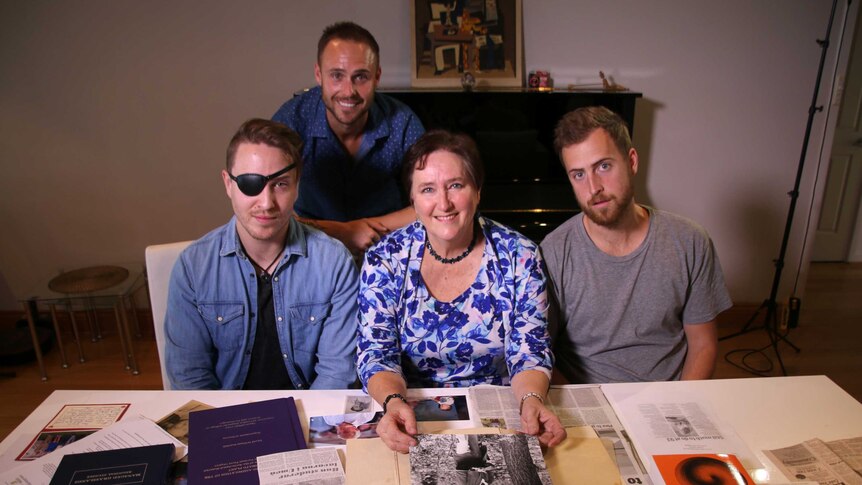 A wide shot showing Karen Goodall-Smith and her three sons smiling for a photo sitting at a table in a living room.