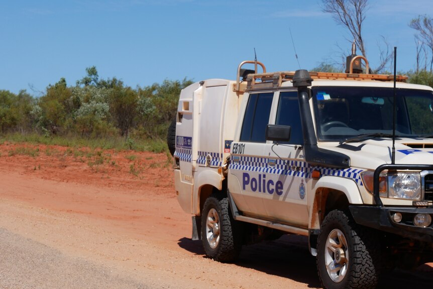 A police car parked at the side of a dirt road.