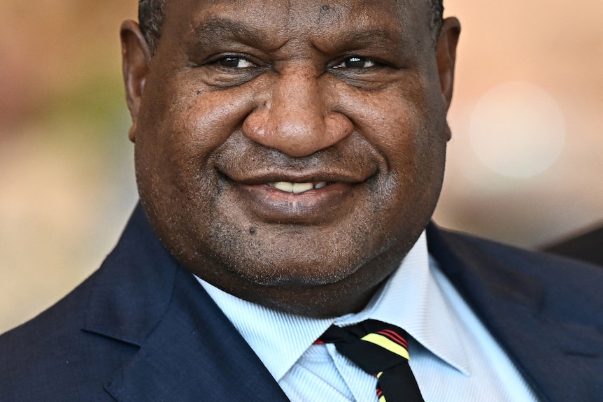 A close up of James Marape smiling while wearing a suit and striped tie.