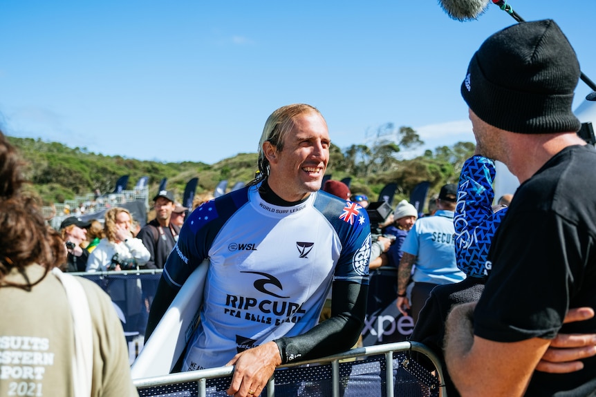 A surfer carrying a surfboard speaks to a fan over a fence after an event in Australia