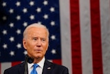 Joe Biden glances to his left in front of a large American flag