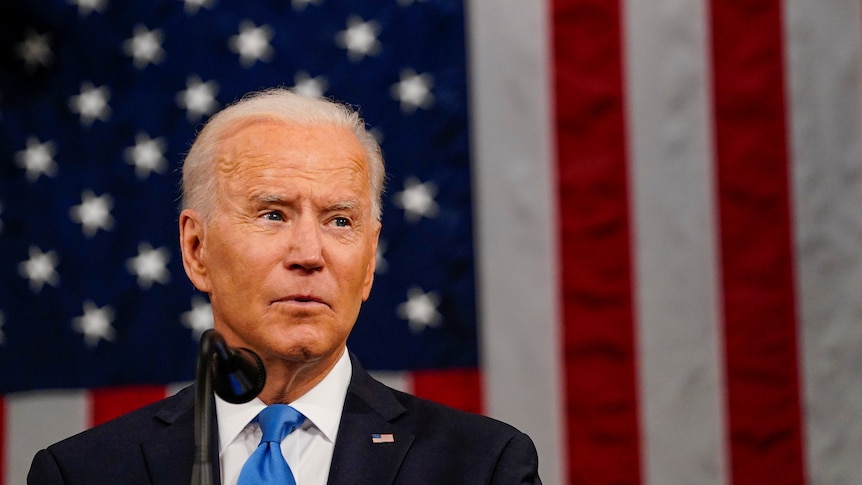 Joe Biden glances to his left in front of a large American flag