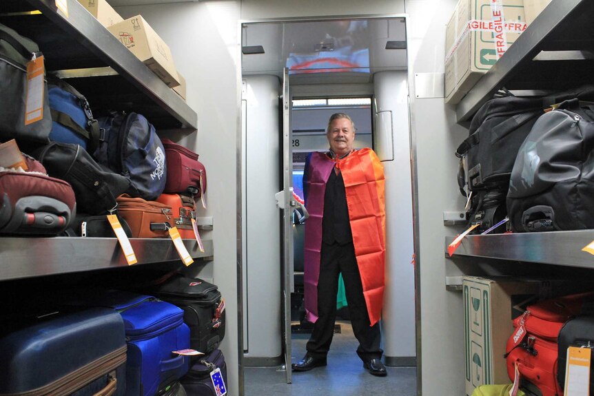 A man stands in a colourful cape in the luggage compartment of a train.