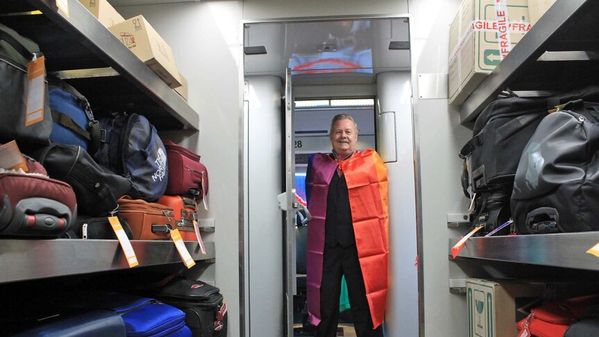 A man stands in a colourful cape in the luggage compartment of a train.