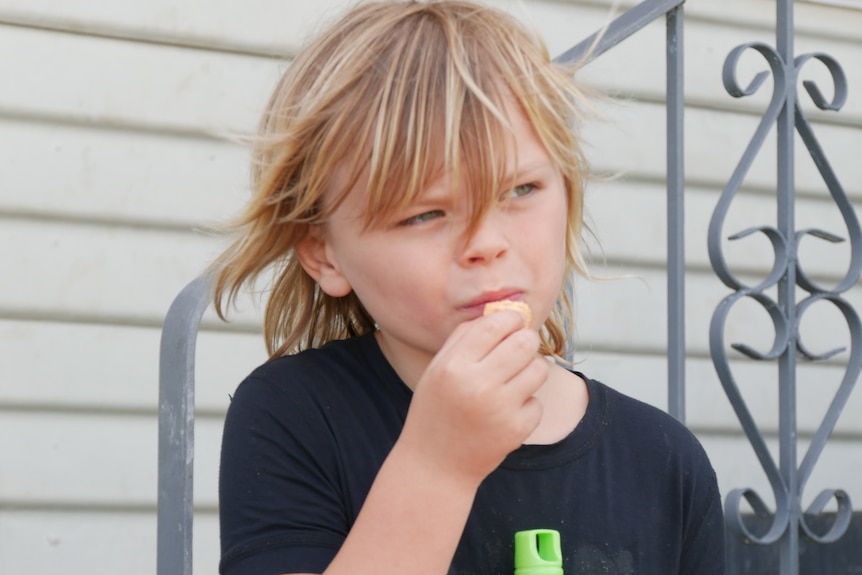 A young boy with blonde hair eats.