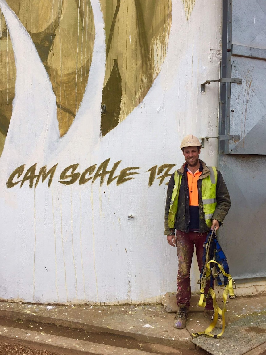 A man in a hard hat stands in front of a wall.