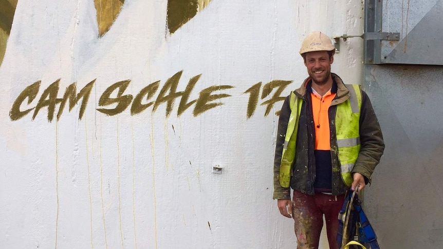 A man in a hard hat stands in front of a wall.