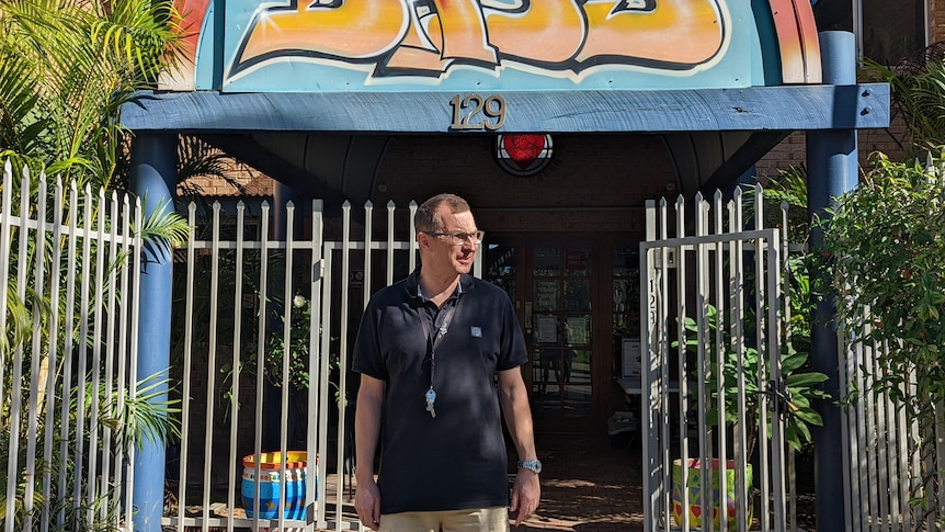Jacob Davis stands outside gate to detox centre wearing polo shirt in front of graffiti sign and plants