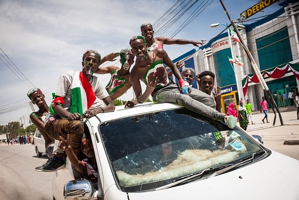 Men painted in colours of Somaliland's flag stick their head out of a car. They are smiling and exuberant.